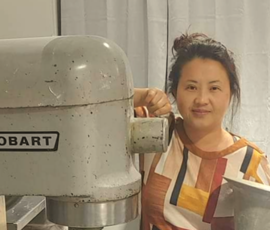 Melinda Vue posing with a commercial Hobart mixer